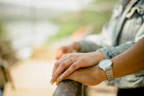 Free Hands of a couple resting on a railing, showcasing an engagement ring and a wristwatch. Stock Photo