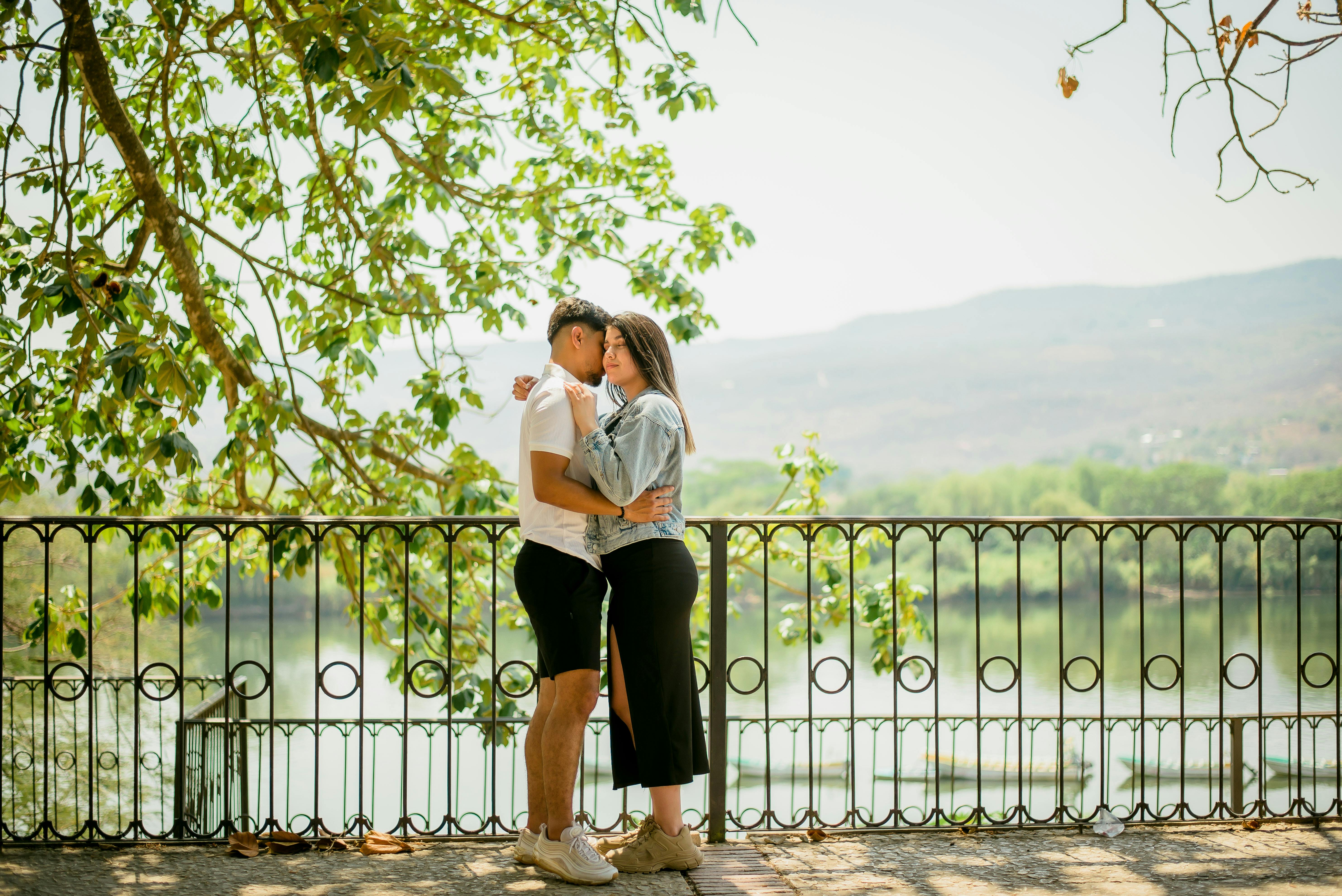 A young couple embraces lovingly by a scenic lake view, surrounded by lush greenery.