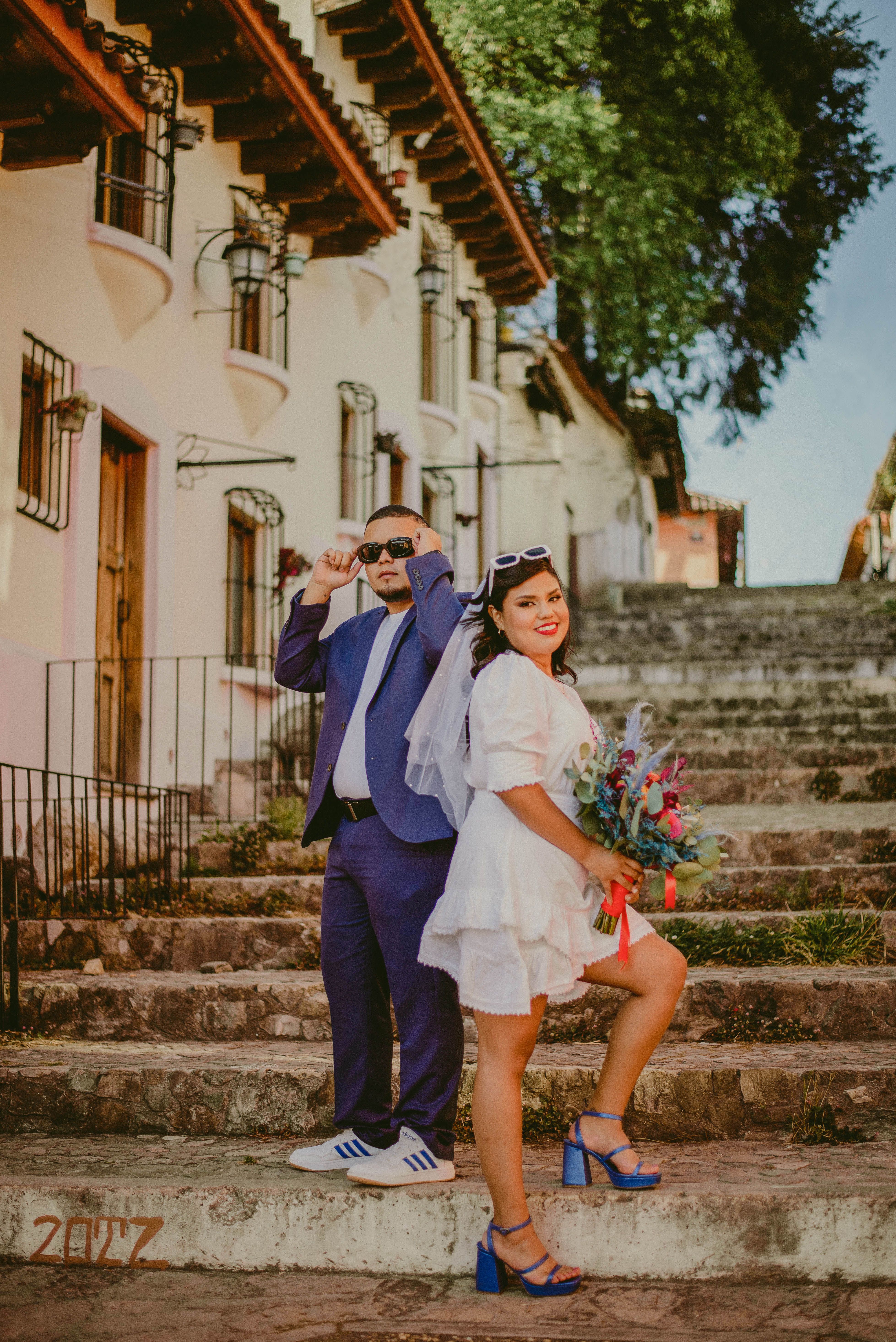 Happy wedding couple posing on rustic stone steps with colorful bouquet.