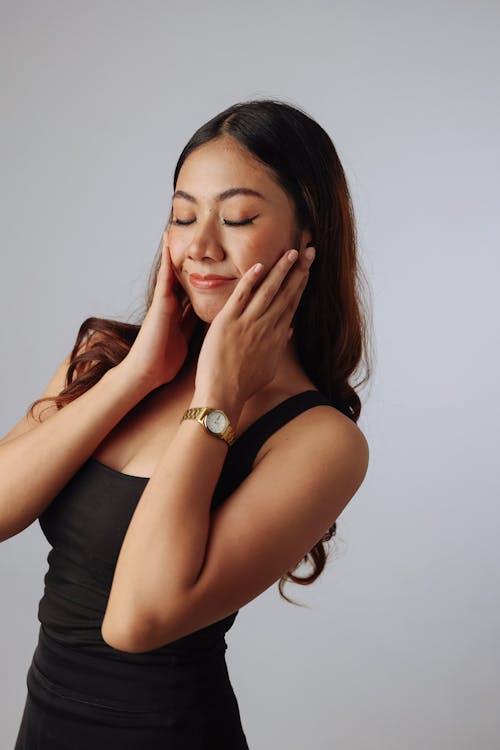 A woman in a black dress is touching her face