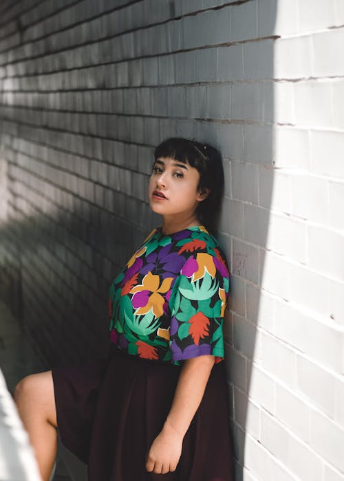 A woman leaning against a wall wearing a colorful top