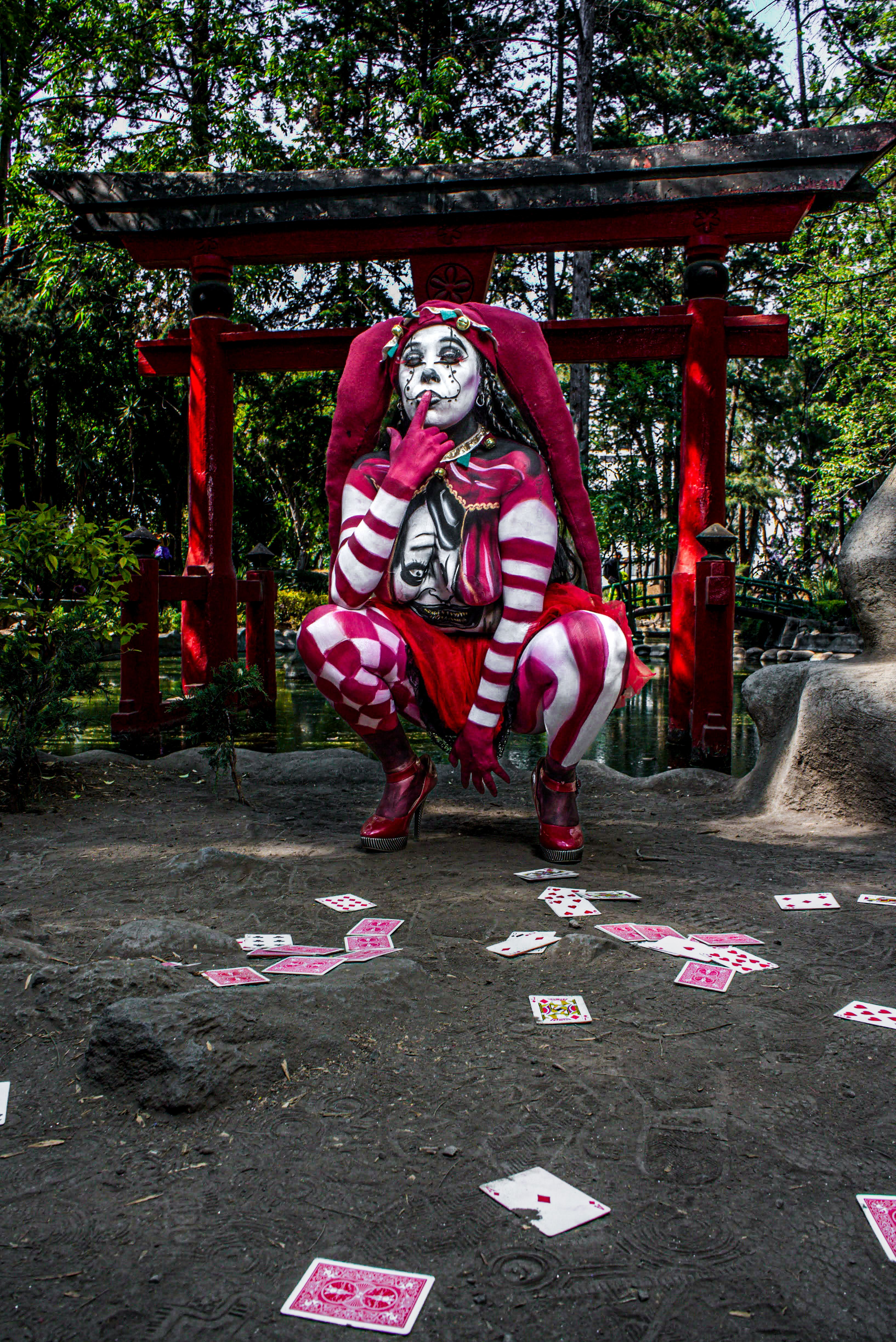 Captivating photo of a woman dressed as a jester, surrounded by playing cards in a Japanese garden.