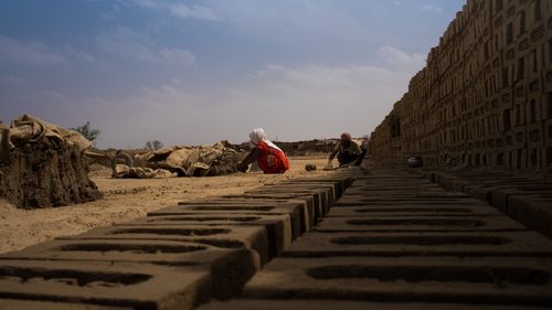 Free Two rural workers making bricks outdoors in a village. Captures a work scene with bricks and mud under a blue sky. Stock Photo