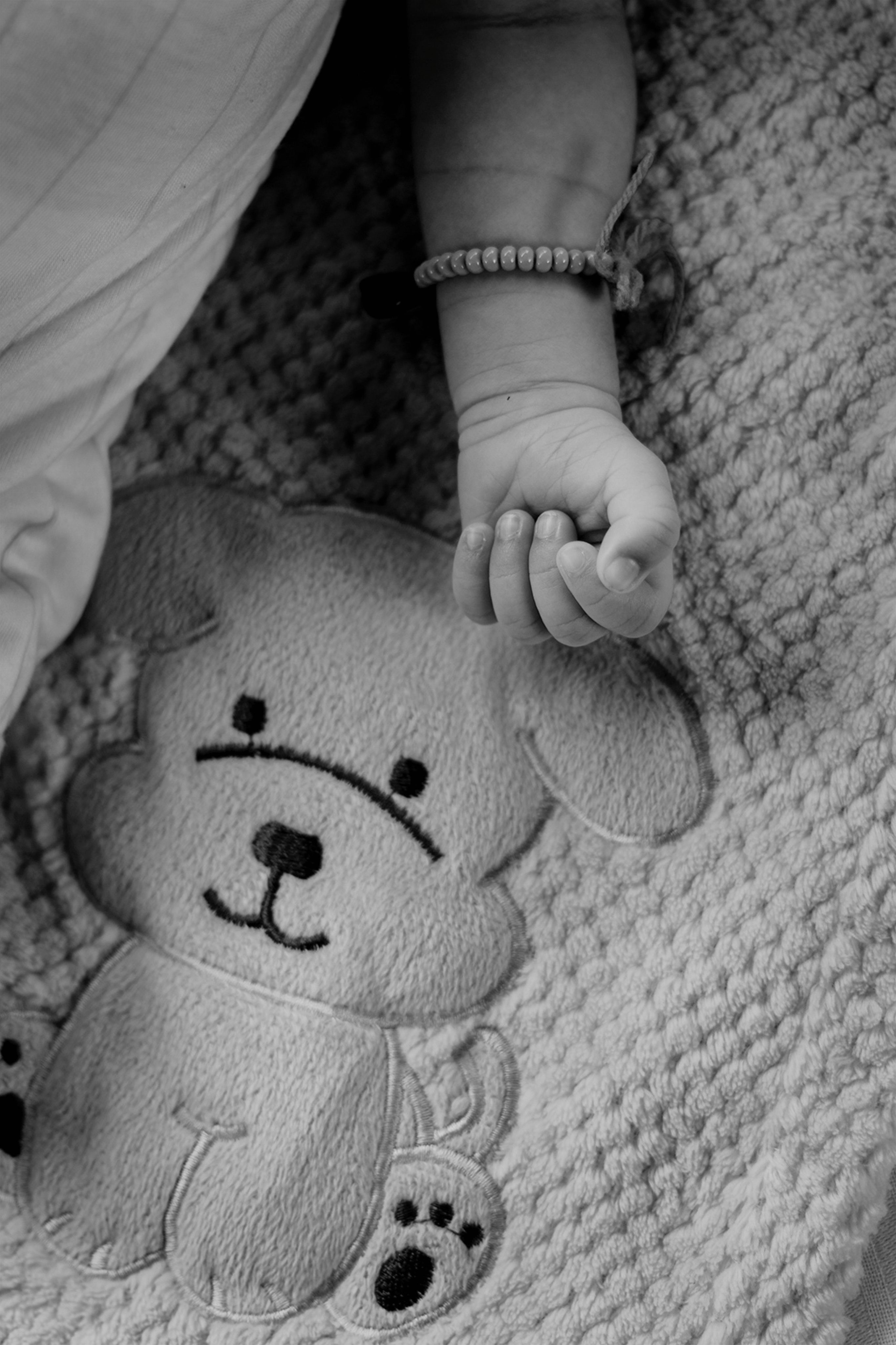 Black and white photo of a baby's hand wearing a bracelet on a textured dog blanket.