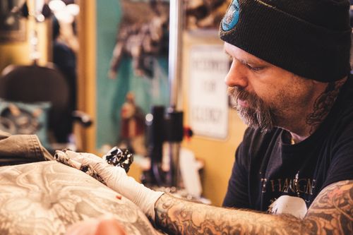 Free Tattoo artist concentrating on creating a detailed tattoo design in a studio setting. Stock Photo