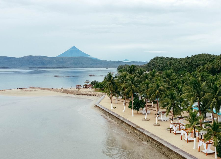 Aerial view capturing the scenic beauty of Mayon Volcano and the tropical coastline in Legazpi City, Philippines.