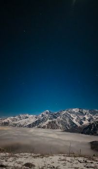 Majestic snowcapped mountains under a clear starry night sky above the clouds.