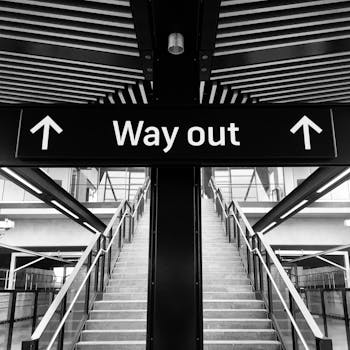 Monochrome image of a staircase with a 'Way Out' sign above, leading to an exit.
