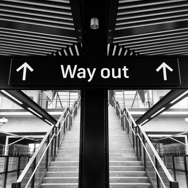 Monochrome image of a staircase with a 'Way Out' sign above, leading to an exit.