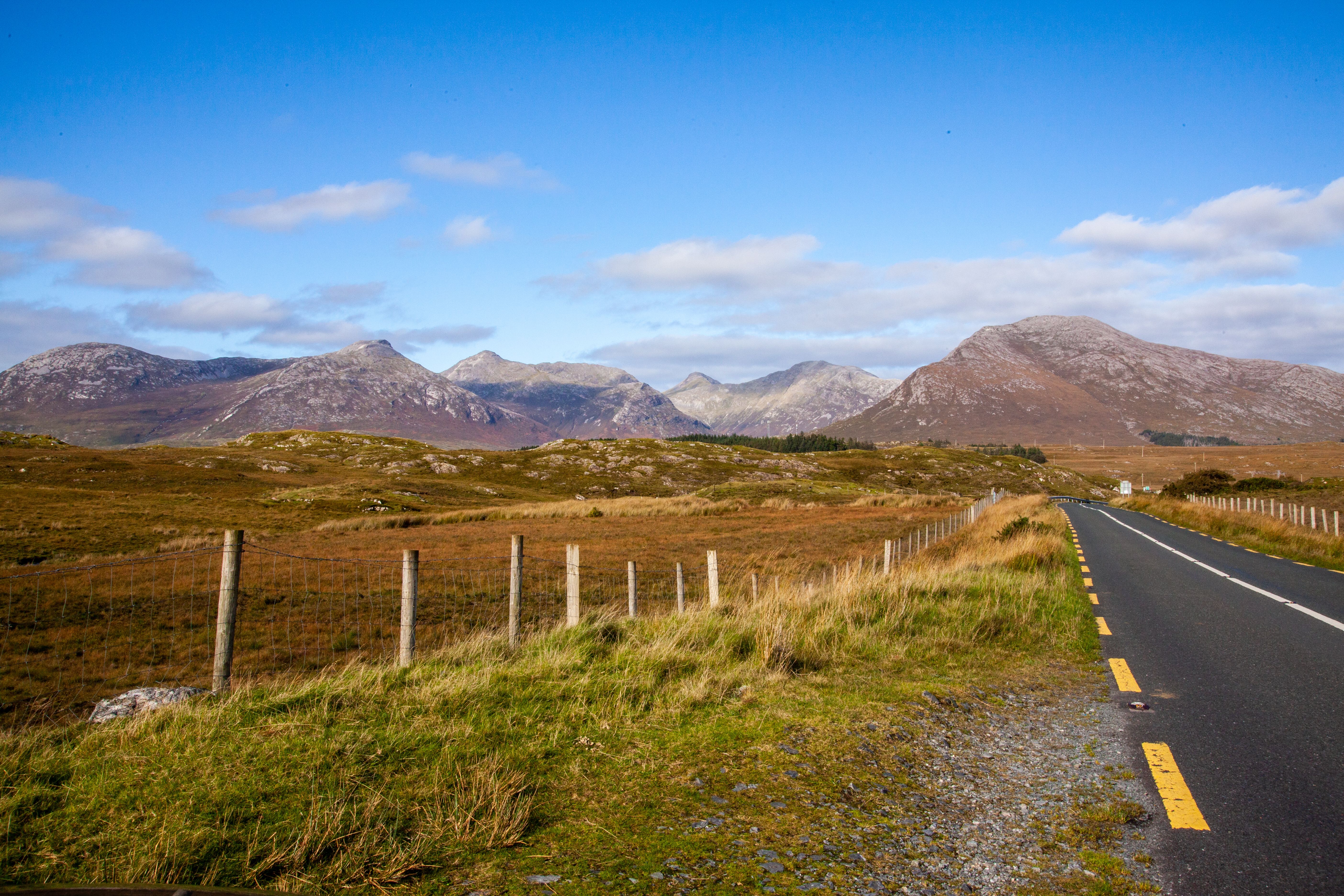 A picturesque rural road with mountains in Connemara, Ireland under a clear blue sky.