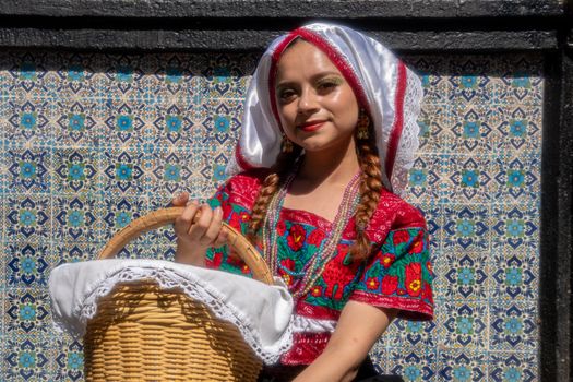 Young woman in Mexican folk costume with a wicker basket, against a colorful wall in Puebla, Mexico.
