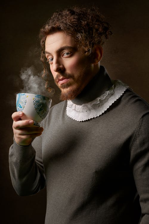 Man Wearing Gray Sweater Holding White and Blue Cup
