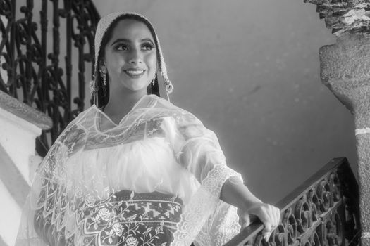 Mexican woman smiling in traditional clothing on ornate staircase.