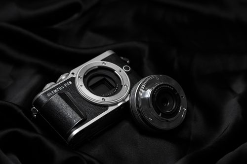 Free Artistic composition of an Olympus Pen camera with lens on black satin fabric. Perfect for photography enthusiasts. Stock Photo