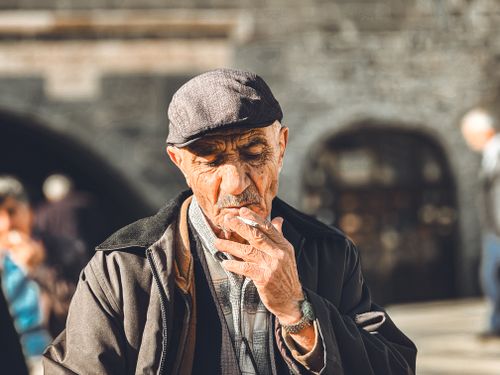 Free Senior man in Diyarbakır, Türkiye, smoking on a sunny day, wearing an ivy cap. Stock Photo