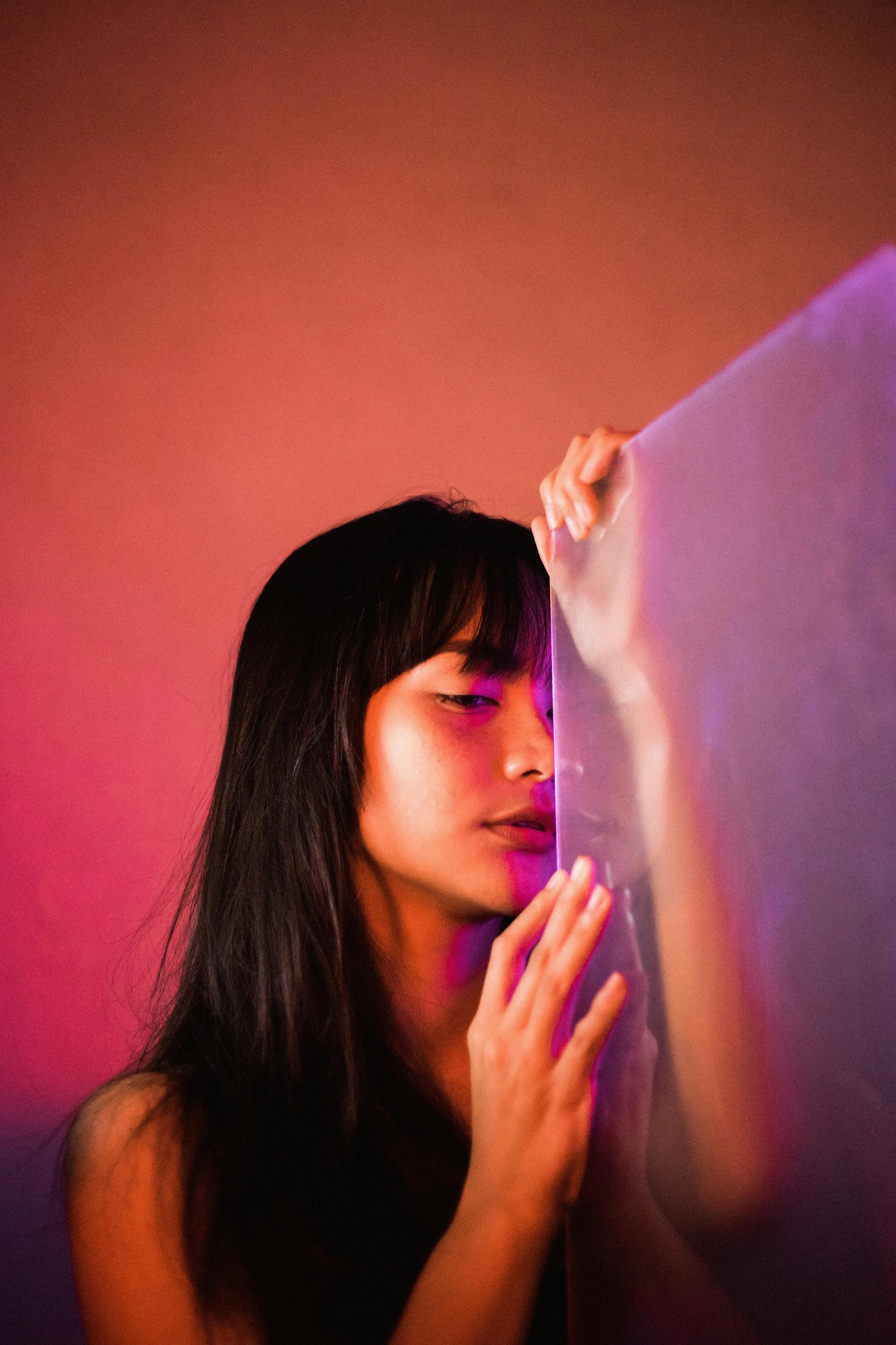 Artistic portrait of a serene woman posing with frosted glass, bathed in soft pink lighting.