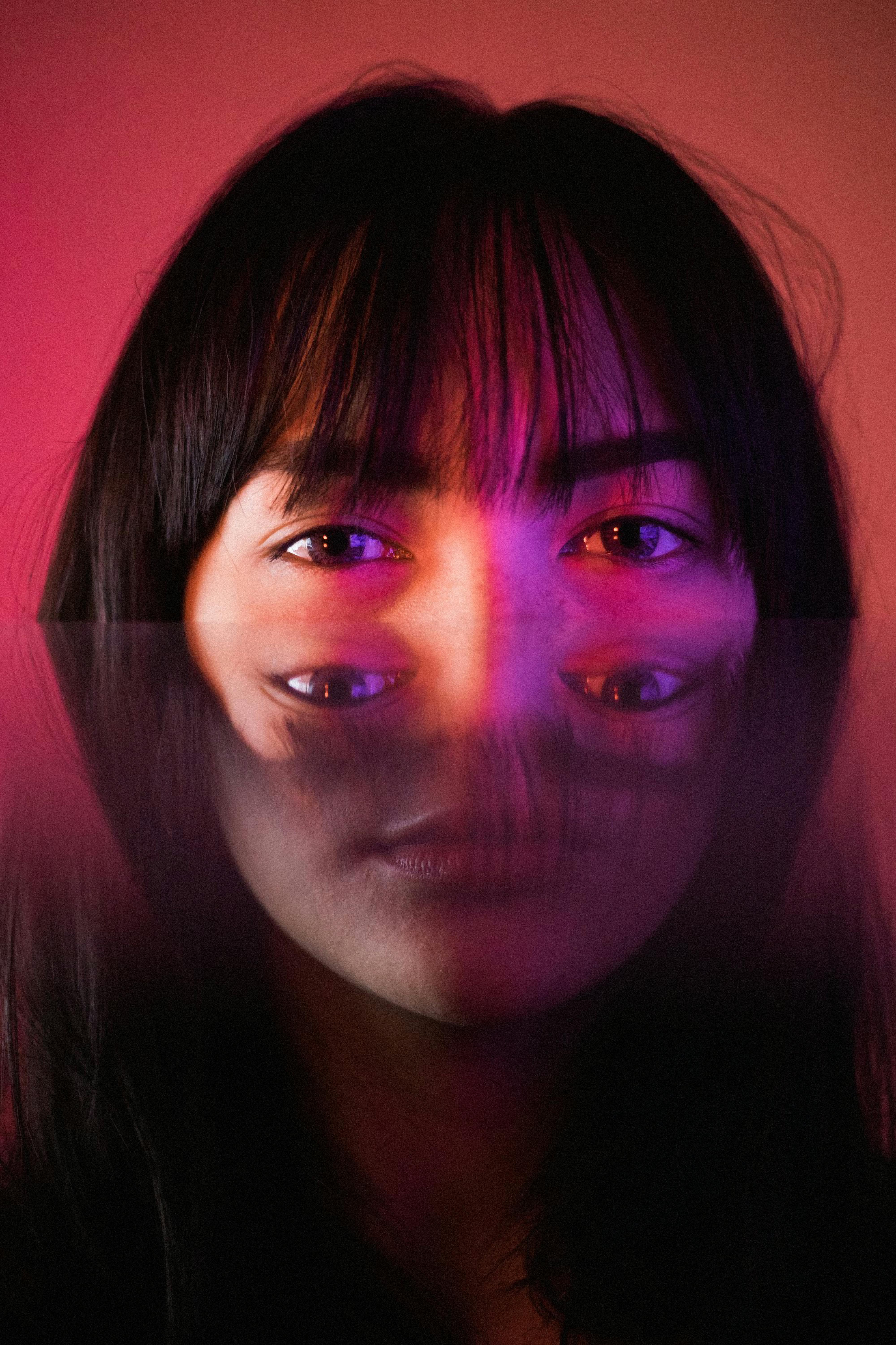 Artistic portrait of a woman using mirror reflection and pink lighting for a surreal effect.