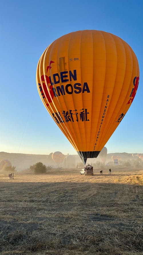 A yellow hot air balloon flying over a field