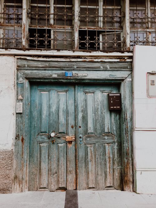 Free A vintage wooden door with a mailbox and barred windows in an old building exterior. Stock Photo