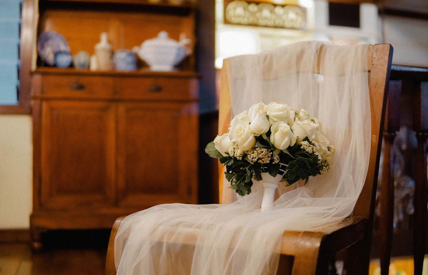 A wedding bouquet of white roses placed on a rustic wooden chair with a delicate veil, perfect for wedding themes.