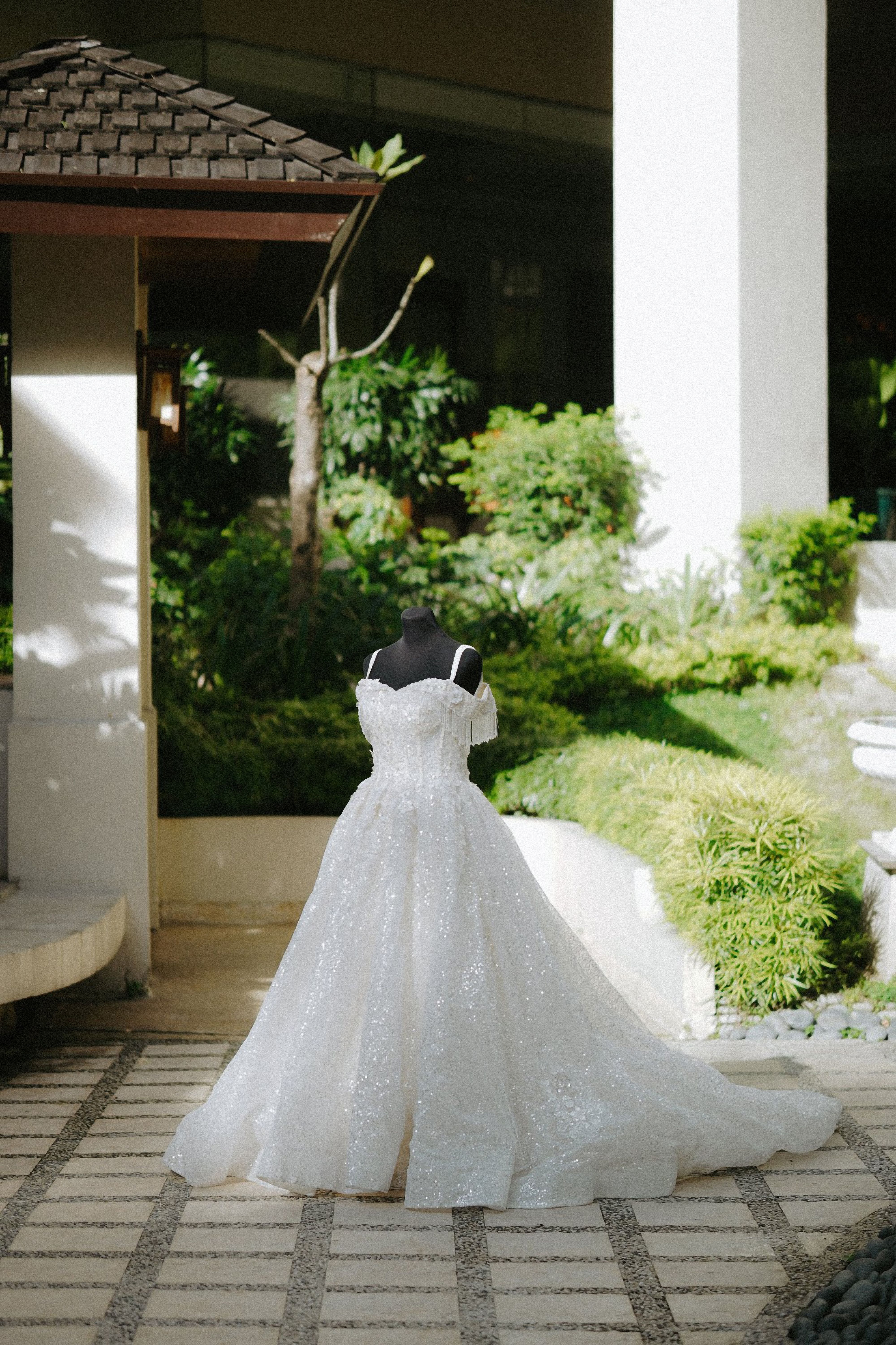 A beautiful white wedding dress displayed on a mannequin in a lush outdoor garden setting.