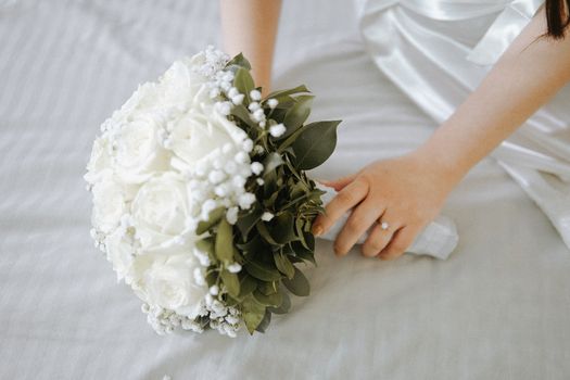 A bride gently holds a bouquet of white roses resting on a satin bed, showcasing elegance and love.