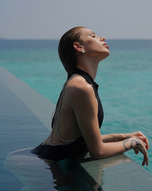 A woman in a black swimsuit sitting on the edge of a pool