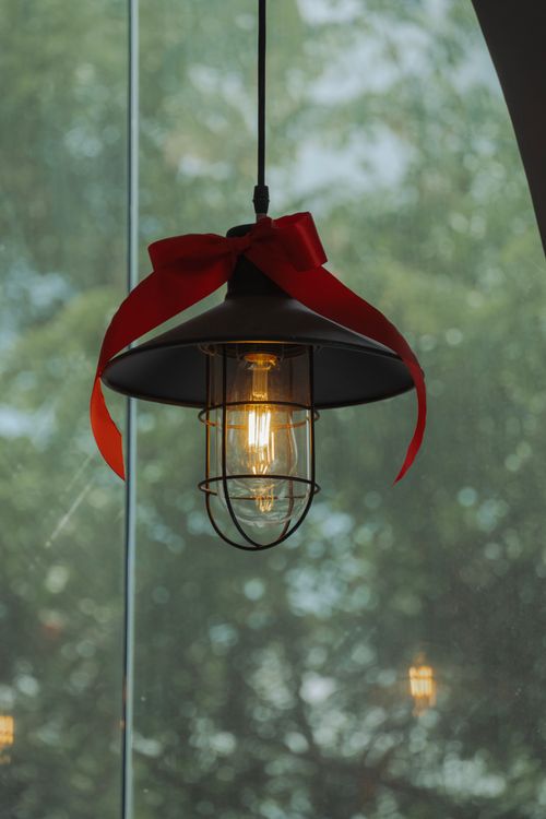 Free A close-up of a hanging lamp with a red ribbon against a blurred outdoor background. Stock Photo