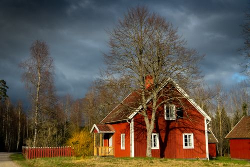 Free A picturesque red house in a serene countryside landscape under dramatic skies. Stock Photo