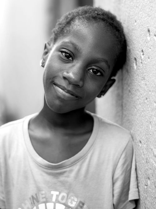 Free Close-up black and white portrait of a smiling child leaning against a wall. Stock Photo