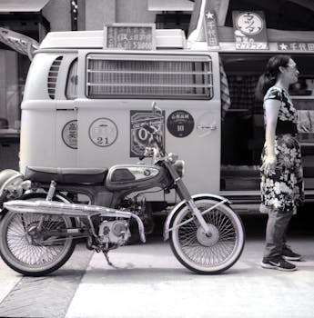 Black and white image of a vintage motorcycle parked near a food truck in Taipei, Taiwan.