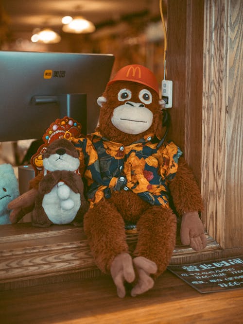 A stuffed monkey wearing a shirt and hat sits on a table