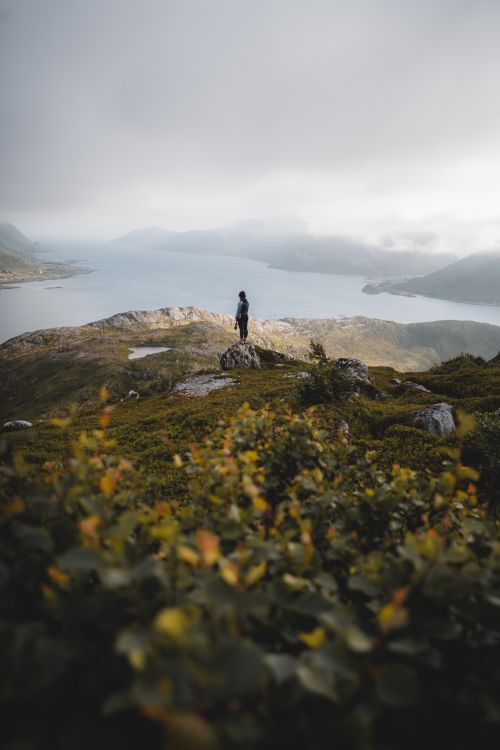 Free A person stands atop a hill, gazing at a tranquil lake surrounded by misty mountains. Stock Photo