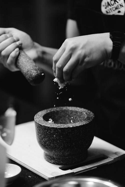 A black and white photo of a person grinding spices