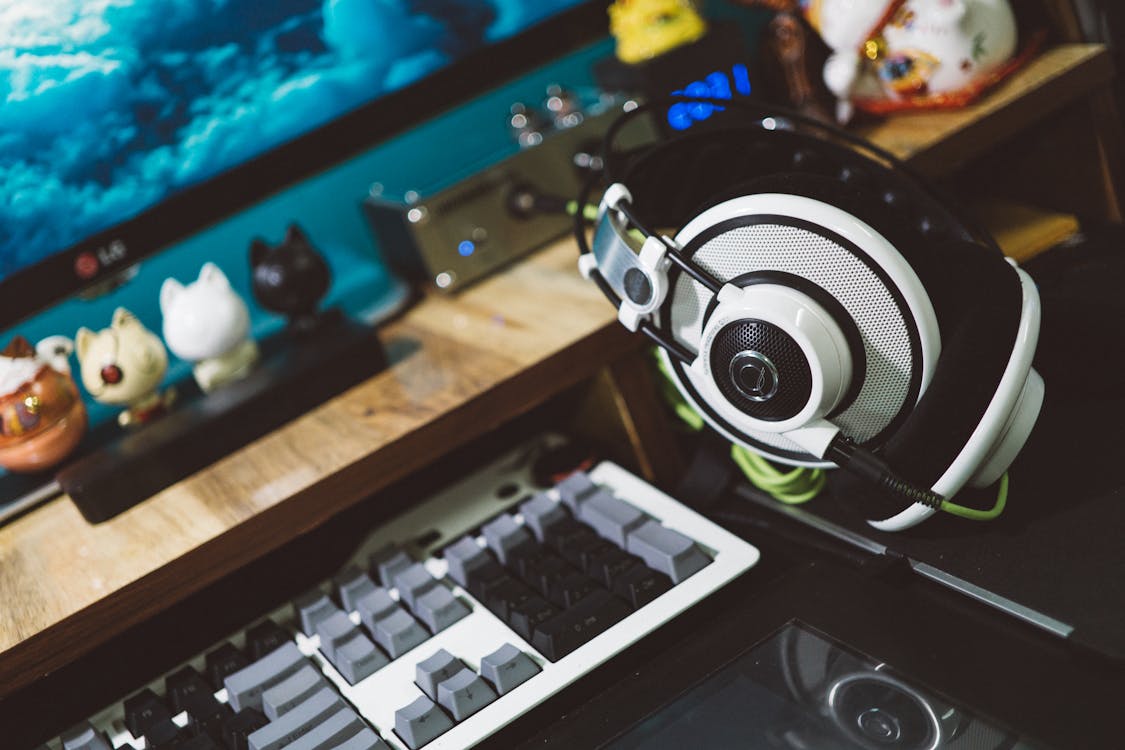 Free A modern desktop setup featuring stylish headphones, keyboard, and decorative figurines for a cozy tech workspace. Stock Photo