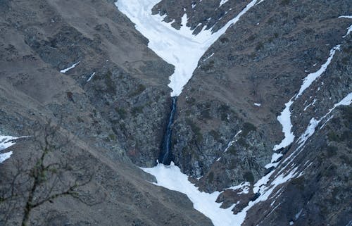 A waterfall is seen in the middle of a snowy mountain