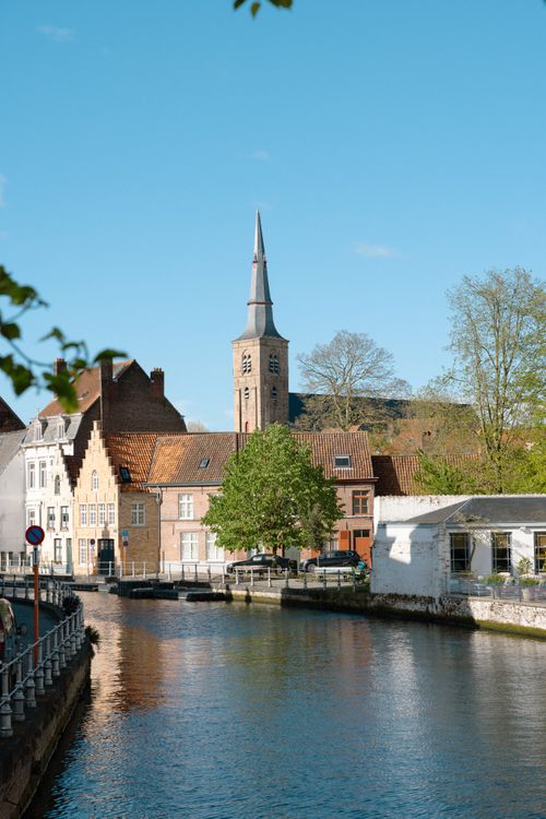 Free Picturesque scene of Bruges with canal, historic buildings, and clear blue sky. Stock Photo