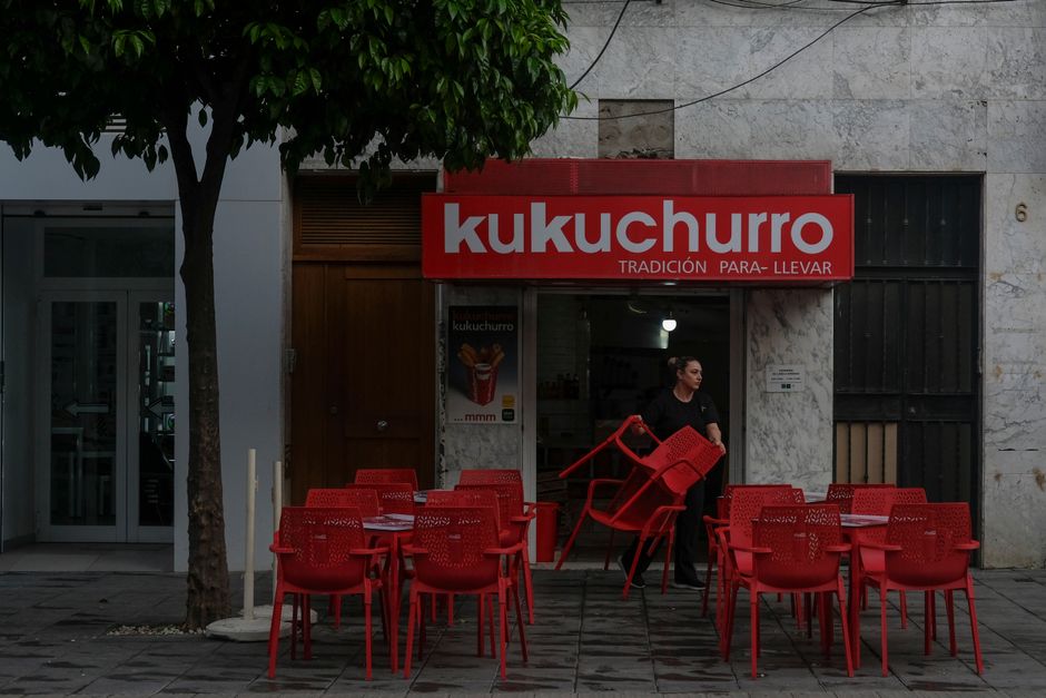 Asientos al aire libre en Kukuchurro, una churrería tradicional en Sevilla, España. Sillas rojas vibrantes y una fachada clásica.