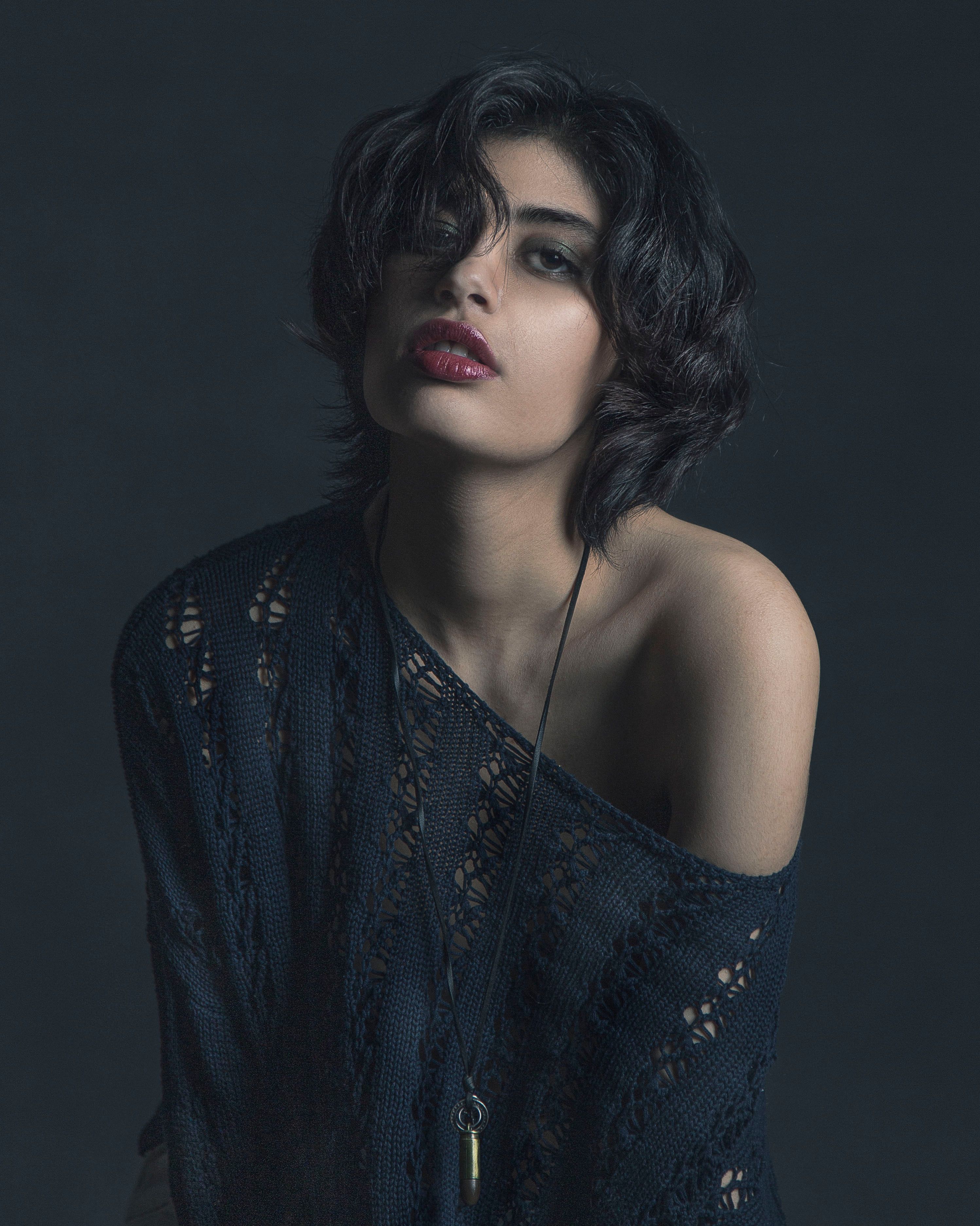 Stunning portrait of a woman with black hair, wearing a black blouse, set against a gray background.