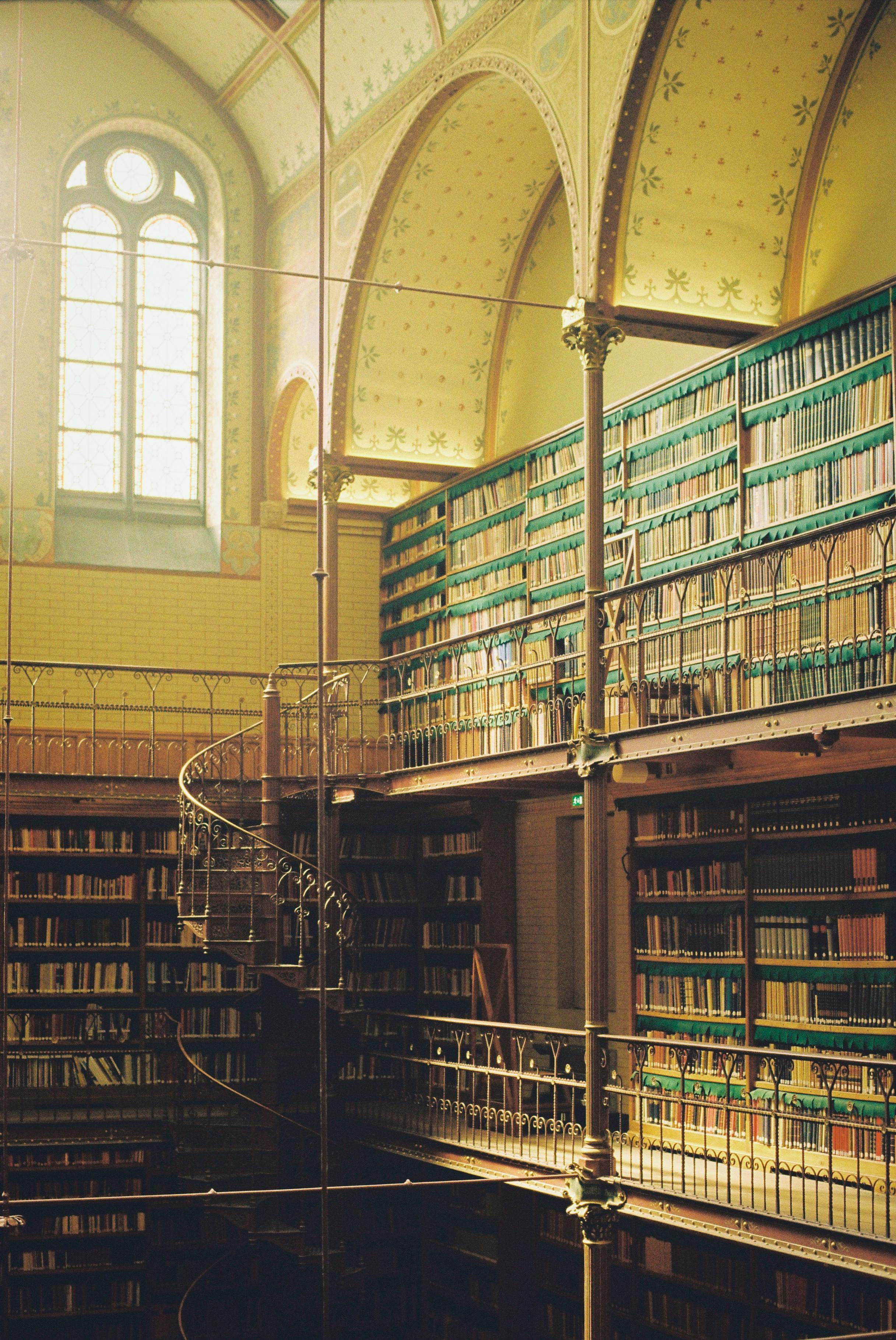 A bright library interior featuring shelves full of books and a spiral staircase.