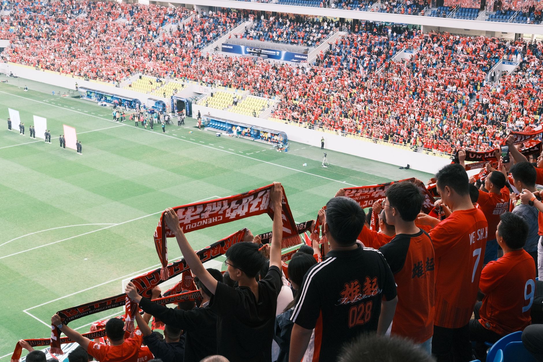 Crowd of soccer supporters in a stadium, waving scarves and cheering during a lively match.