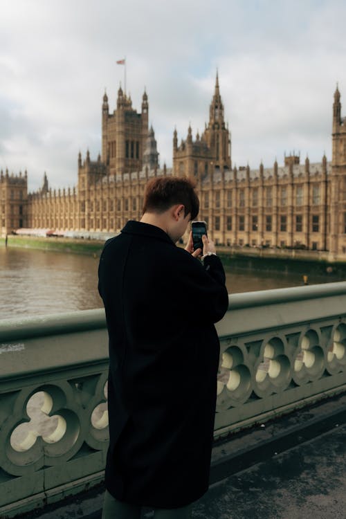 Man in Black Coat Taking Pictures of Westminster Palace