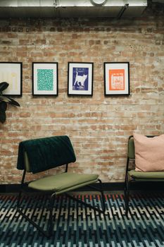 Stylish interior with chairs and vibrant artwork on exposed brick wall, London.