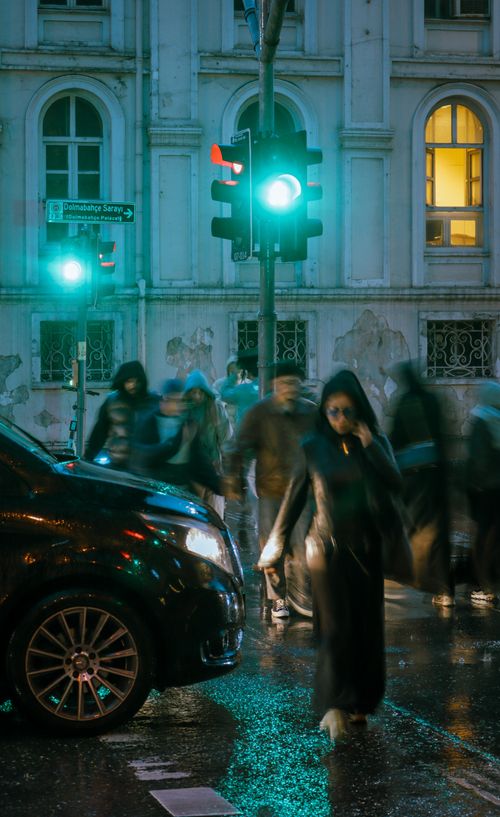 Free A busy city street with blurred pedestrians crossing under green lights on a rainy night. Stock Photo