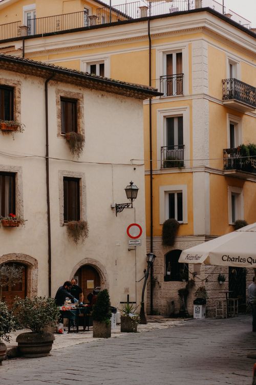 Free A quaint European street with people dining at a café under warm sunlight. Stock Photo