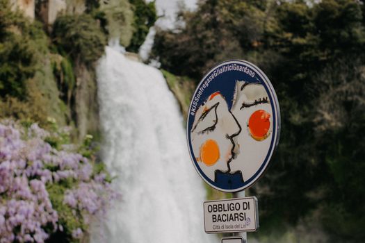 A road sign in front of Cascata Grande waterfall in Isola del Liri, Italy, promoting affection.