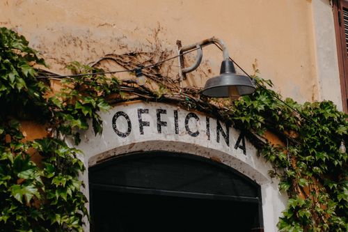 Free Vintage Italian building facade with ivy and rustic lamp above 'Officina' sign. Stock Photo