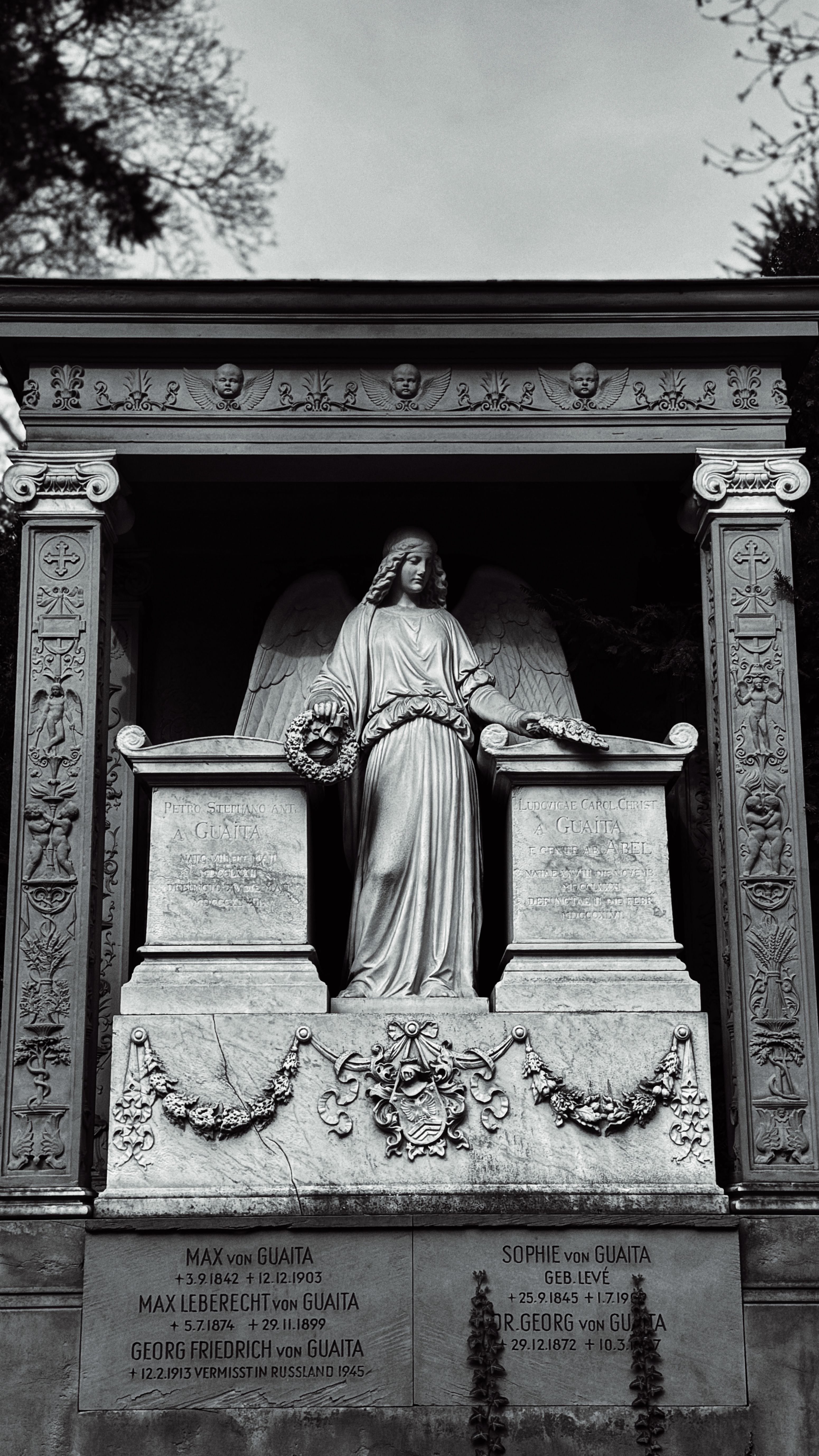 Intricate angel statue at Frankfurt cemetery, showcasing detailed craftsmanship in a serene setting.