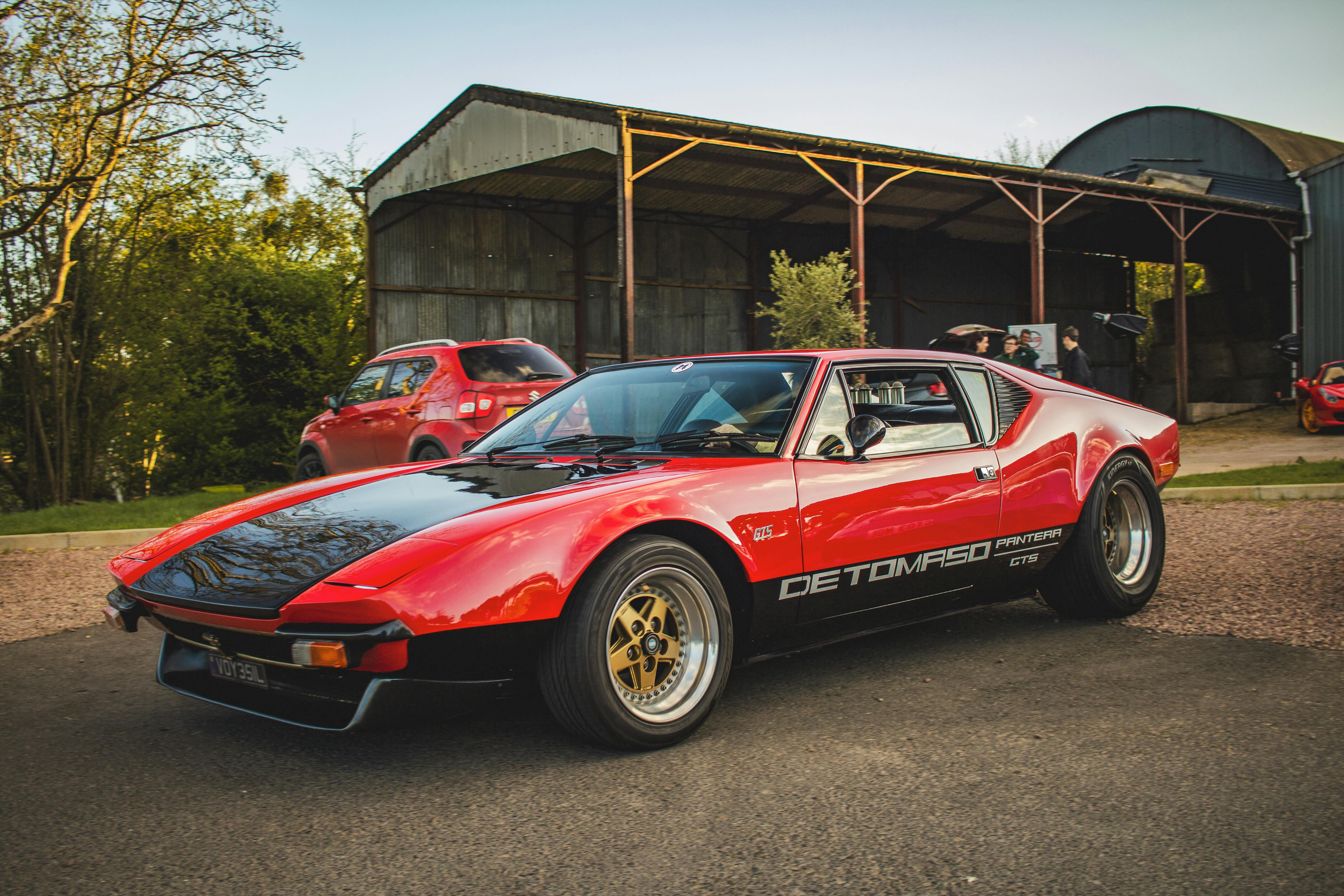A red and black sports car parked in front of a barn