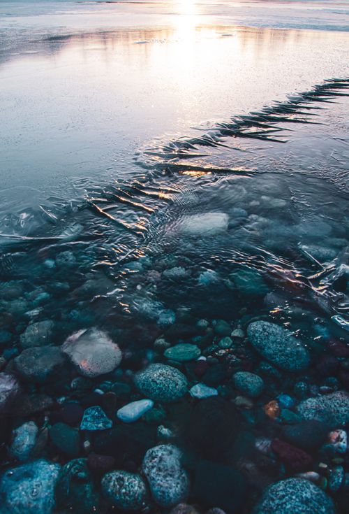 Free A serene twilight scene of a frozen shore with visible pebbles and soft reflections, capturing winter's beauty. Stock Photo